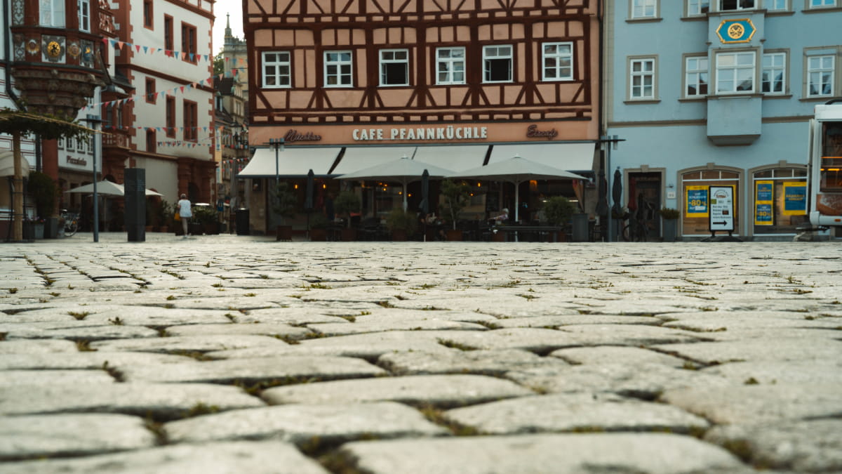 Bodentiefe Aufnahme des historischen Kopfsteinpflasters auf dem Coburger Marktplatz mit Fachwerkhäusern im Hintergrund – Referenzprojekt von Christian Knoch Tiefbau.